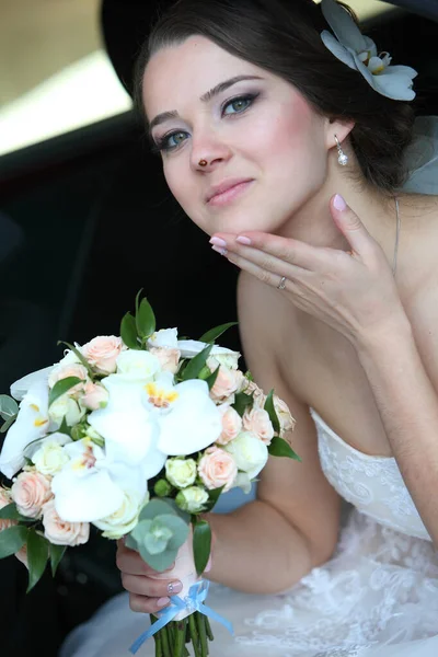 A bride with a bouquet in her hand and a ladybird on her nose in a car in the back seat.