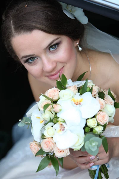 Cute bride with a bouquet in her hand in a car in the back seat