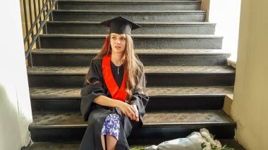 Merdivenli bir kadın mezuniyet portresi. Usta kız merdivenlerde oturuyor.