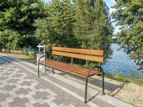 Trä park bänk med en soptunna på bakgrunden av träd och floden Dnepr i Kiev. — Stockfoto