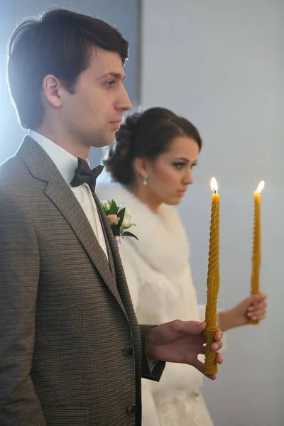 Panna młoda i pan młody na ceremonii ślubnej. Szczęśliwy stylowy ślub para gospodarstwa świece ze światłem pod złote korony podczas świętego małżeństwa w kościele. — Zdjęcie stockowe
