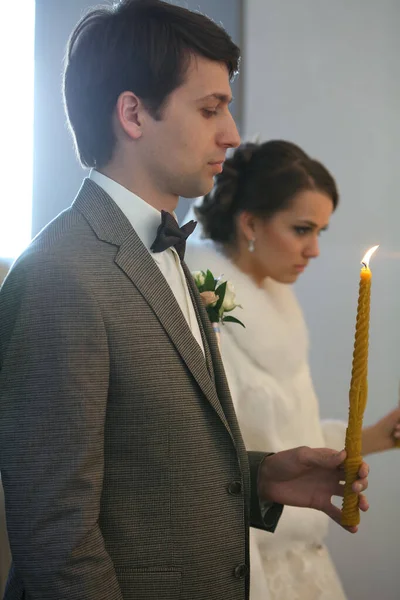 Panna młoda i pan młody na ceremonii ślubnej. Szczęśliwy stylowy ślub para gospodarstwa świece ze światłem pod złote korony podczas świętego małżeństwa w kościele. — Zdjęcie stockowe