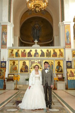 Gelin ve damat düğün töreninde. Kilisedeki kutsal evlilik töreninde altın taçların altında mum tutan mutlu bir düğün çifti..