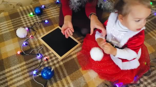 Mor med datter på tavlen tegne julen attributter. Mor og datter tegner et juletræ. Jul tema: mor og datter male jul i en hjemlig festlig indstilling. – Stock-video