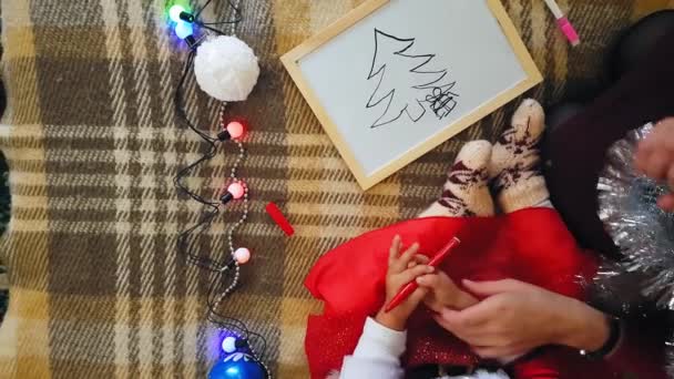 Mamá con hija en la pizarra dibuja atributos navideños. Mamá y su hija están dibujando un árbol de Navidad. Tema de Navidad: mamá e hija pintan Navidad en un ambiente festivo hogareño . — Vídeo de stock