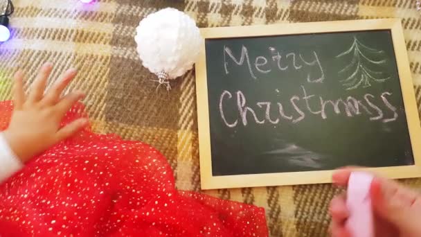 Mama z córką w zarządzie rysują świąteczne atrybuty. Mama i córka rysują choinkę. Temat Bożego Narodzenia: mama i córka malować Boże Narodzenie w domowym świątecznym otoczeniu. — Wideo stockowe