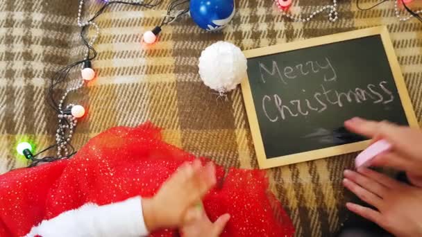 Mamá con hija en la pizarra dibuja atributos navideños. Mamá y su hija están dibujando un árbol de Navidad. Tema de Navidad: mamá e hija pintan Navidad en un ambiente festivo hogareño . — Vídeos de Stock