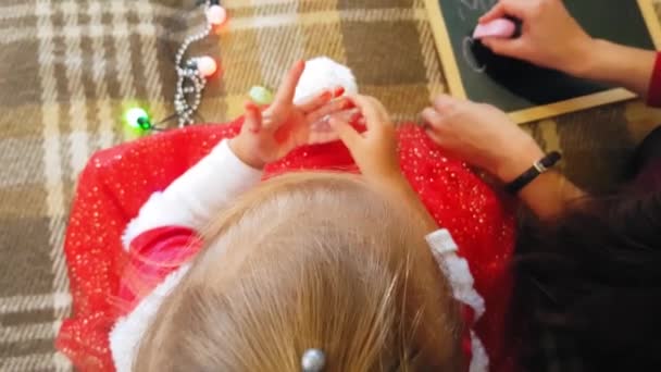 Mamá con hija en la pizarra dibuja atributos navideños. Mamá y su hija están dibujando un árbol de Navidad. Tema de Navidad: mamá e hija pintan Navidad en un ambiente festivo hogareño . — Vídeos de Stock