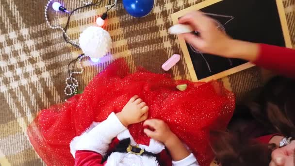 Мама і дочка малюють новорічні атрибути на дошці. Мама з донькою малюють ялинку. Новорічна тема: мама і дочка малюють новий рік у домашній святковій атмосфері.. — стокове відео