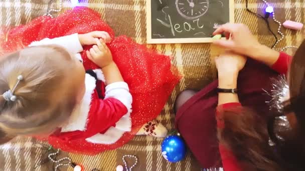 Mutter und Tochter malen Neujahrsattribute auf die Tafel. Mutter und Tochter malen einen Weihnachtsbaum. Neujahrsmotto: Mutter und Tochter malen das neue Jahr in festlicher Atmosphäre. — Stockvideo