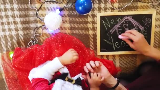 Mutter und Tochter malen Neujahrsattribute auf die Tafel. Mutter und Tochter malen einen Weihnachtsbaum. Neujahrsmotto: Mutter und Tochter malen das neue Jahr in festlicher Atmosphäre. — Stockvideo