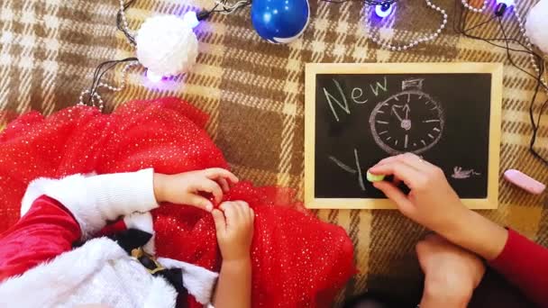 Mamá y su hija dibujan atributos de Año Nuevo en la pizarra. Mamá y su hija están dibujando un árbol de Navidad. Tema de Año Nuevo: mamá y su hija pintan el año nuevo en un ambiente festivo en casa . — Vídeos de Stock