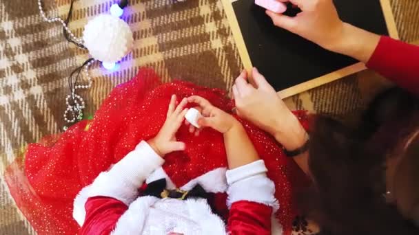 Anya és lánya újévi jellemzőket rajzolnak a táblára. Anya és lánya karácsonyfát rajzolnak. Újévi téma: anya és lánya festik az új évet ünnepi hangulatban. — Stock videók
