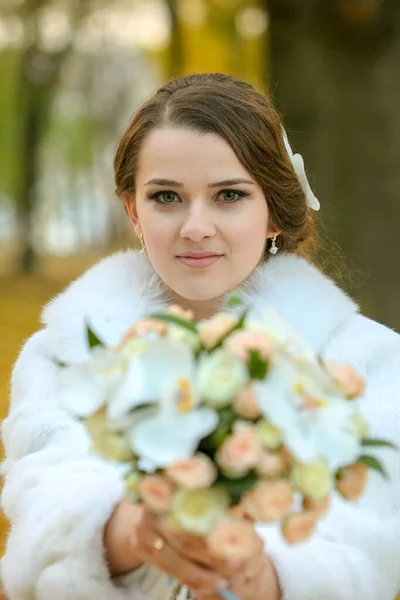 Nevěsta s kyticí květin v podzimním parku v bílém kožichu — Stock fotografie