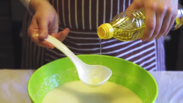 Närbild slow motion av en kvinnlig hand lägger solrosolja till smet i en grön skål i köket. Matlagning pannkakor — Stockvideo
