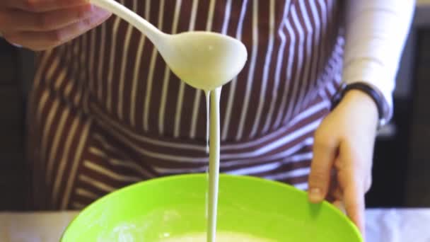 Gros plan Le mouvement lent d'une main féminine mélange une pâte avec une cuillère en plastique blanc dans un bol vert dans la cuisine de la maison. Crêpes de cuisson — Video