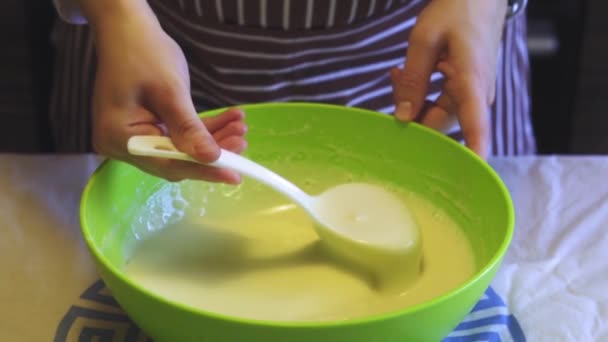 Primer plano cámara lenta de una mano femenina mezcla una masa con una cuchara de plástico blanco en un tazón verde en la cocina del hogar. Panqueques de cocina — Vídeo de stock