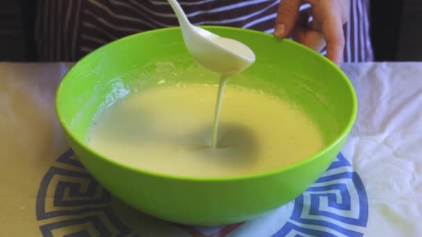 Close-up câmera lenta de uma mão feminina mistura uma massa com uma colher de plástico branco em uma tigela verde na cozinha da casa. Panquecas de cozinha — Vídeo de Stock