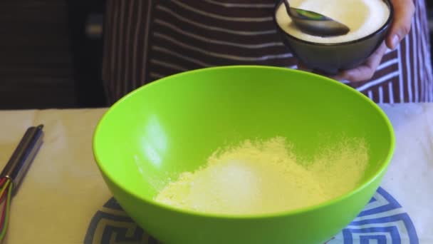 Close-up câmera lenta de uma mão feminina adiciona açúcar à farinha em uma tigela verde na cozinha da casa. Panquecas de cozinha — Vídeo de Stock
