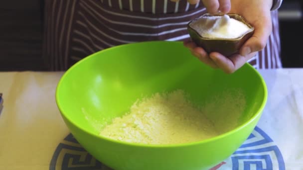 Крупным планом замедленное движение женской руки добавляет соль в муку в зеленой миске на домашней кухне. Блинчики для готовки — стоковое видео