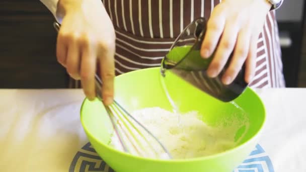 Крупный план женской руки добавляет воды в муку в зеленой миске на домашней кухне. Блинчики для готовки — стоковое видео