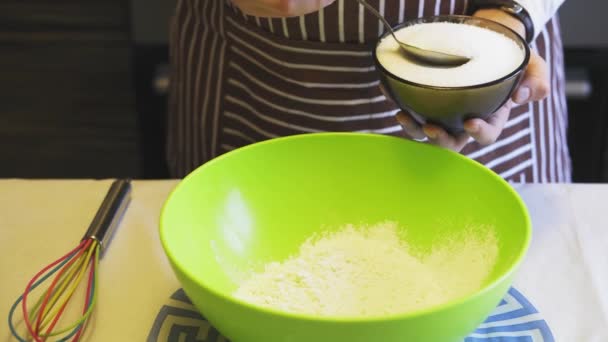 Крупним планом жіноча рука додає цукор до борошна в зеленій мисці на домашній кухні. Приготування млинців — стокове відео