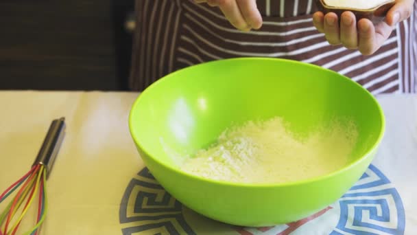 Крупный план женской руки добавляет соль к муке в зеленую миску на домашней кухне. Блинчики для готовки — стоковое видео