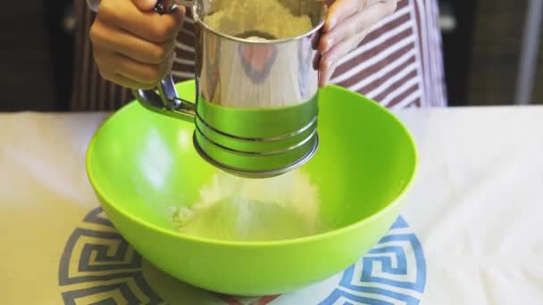 Gros plan d'une femme tamisant à la main de la farine avec une tasse de tamis dans un bol vert dans la cuisine de la maison. Crêpes de cuisson — Video