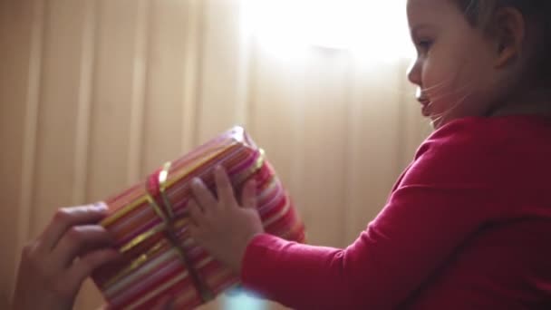 Close-up van een klein meisje in een rode jas met een doos met een geschenk in haar handen en zoenen haar moeder — Stockvideo