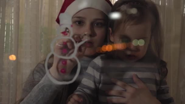 Maman et fille dessinent un bonhomme de neige avec de la peinture sur une vitre. Dessin avec acrylique sur verre . — Video