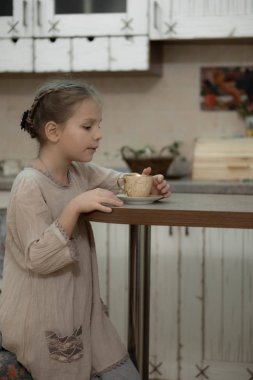 Koyu sarı, bej elbiseli kız mutfakta çay içiyor.