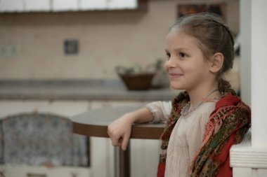 Bej elbiseli esmer bir kız ve mutfakta omzundan sarkan renkli bir eşarp.