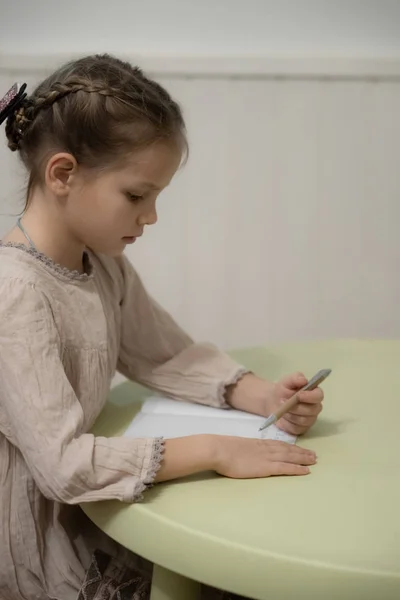 Una chica rubia oscura con un vestido beige está haciendo la tarea — Foto de Stock