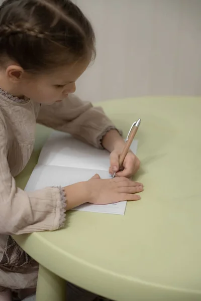 Uma garota loira escura em um vestido bege está fazendo lição de casa — Fotografia de Stock