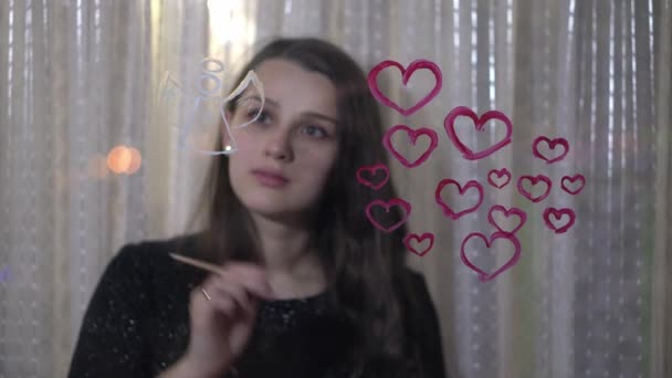 Vacker flicka målar hjärta och ängel på glas — Stockvideo