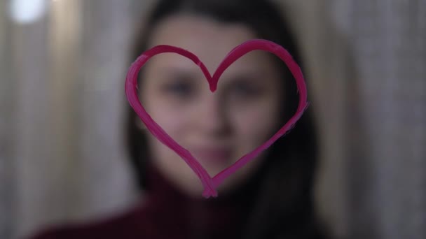Красивая девушка рисует сердце на стекле — стоковое видео