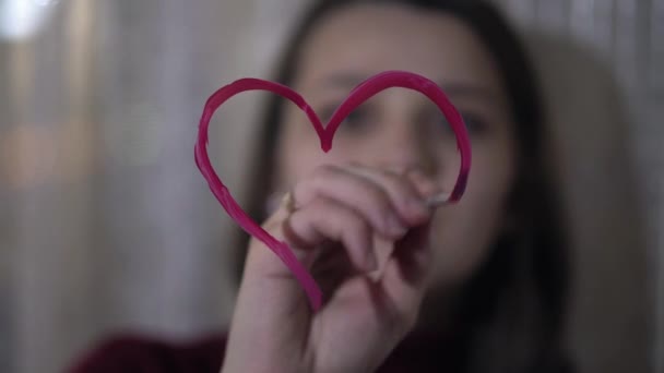 Красивая девушка рисует сердце на стекле — стоковое видео