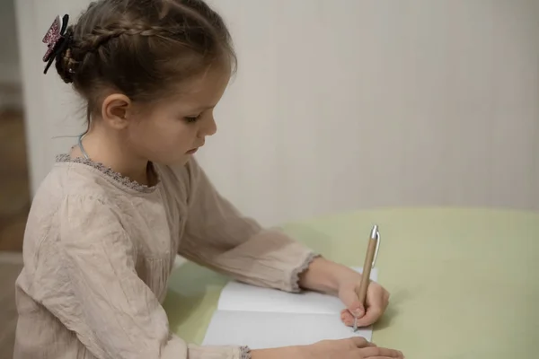 Een donker blond meisje in een beige jurk doet huiswerk — Stockfoto