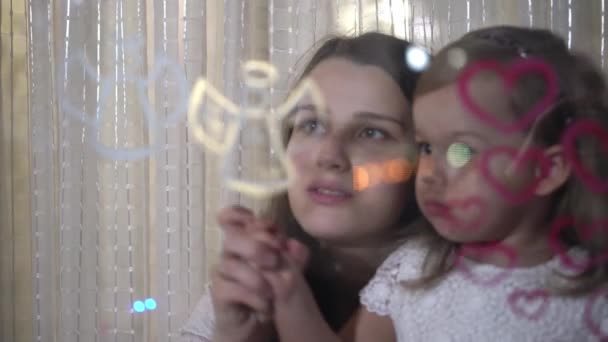 Mamá con hija pequeña dibujar el corazón y pinturas ángel en vidrio . — Vídeo de stock