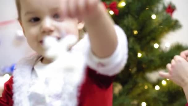 赤ちゃんと妊娠中のママはクリスマスツリーに赤いボールのおもちゃを掛けます。幸せな子供時代のコンセプト。子供と母親はクリスマスボールで木を飾る。小さな子供と親がクリスマスツリーで遊んでいます. — ストック動画