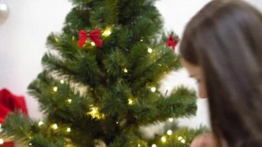 Bebek ve hamile bir anne Noel ağacına kırmızı top oyuncağı asıyor. Mutlu çocukluk kavramı. Çocuk ve anne Noel toplarıyla ağacı süslerler. Küçük çocuk ve bir ebeveyn Noel ağacının yanında oynuyorlar..