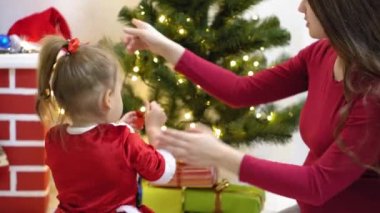 Bebek ve hamile bir anne Noel ağacına kırmızı top oyuncağı asıyor. Mutlu çocukluk kavramı. Çocuk ve anne Noel toplarıyla ağacı süslerler. Küçük çocuk ve bir ebeveyn Noel ağacının yanında oynuyorlar..
