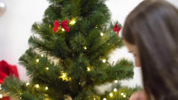 Baby und schwangere Mutter hängen rotes Kugelspielzeug an den Weihnachtsbaum. Glückliche Kindheit. Kind und Mutter schmücken Baum mit Weihnachtskugeln. Kleines Kind und ein Elternteil spielen am Weihnachtsbaum. — Stockvideo