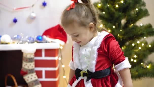 엄마와 아기가 크리스마스 트리에 빨간 공 장난감을 걸었어요. 행복 한 어린 시절의 컨셉. 아이와 엄마가 크리스마스 때 공으로 나무를 장식하는 거야. 어린 아이와 부모님이 크리스마스 트리에서 연주를 하고 있습니다. — 비디오
