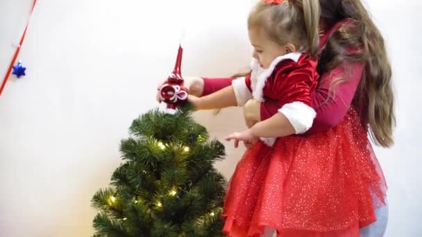 Το μωρό και η έγκυος μαμά κρέμονται κόκκινο παιχνίδι μπάλα στο χριστουγεννιάτικο δέντρο. Χαρούμενη παιδική ιδέα. παιδί και μητέρα διακοσμούν δέντρο με μπάλες Χριστουγέννων. Ένα μικρό παιδί και ένας γονιός παίζουν δίπλα στο χριστουγεννιάτικο δέντρο.. — Αρχείο Βίντεο