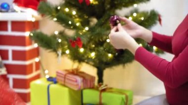 Bebek ve hamile bir anne Noel ağacına kırmızı top oyuncağı asıyor. Mutlu çocukluk kavramı. Çocuk ve anne Noel toplarıyla ağacı süslerler. Küçük çocuk ve bir ebeveyn Noel ağacının yanında oynuyorlar..