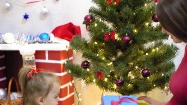 Bebek ve hamile bir anne Noel ağacına kırmızı top oyuncağı asıyor. Mutlu çocukluk kavramı. Çocuk ve anne Noel toplarıyla ağacı süslerler. Küçük çocuk ve bir ebeveyn Noel ağacının yanında oynuyorlar..