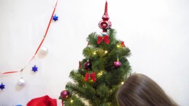 Bebek ve hamile bir anne Noel ağacına kırmızı top oyuncağı asıyor. Mutlu çocukluk kavramı. Çocuk ve anne Noel toplarıyla ağacı süslerler. Küçük çocuk ve bir ebeveyn Noel ağacının yanında oynuyorlar..