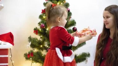 Bebek ve hamile bir anne Noel ağacına kırmızı top oyuncağı asıyor. Mutlu çocukluk kavramı. Çocuk ve anne Noel toplarıyla ağacı süslerler. Küçük çocuk ve bir ebeveyn Noel ağacının yanında oynuyorlar..