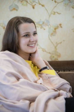 Hoş ve düşünceli bir kızın resmi kanepede oturur ve kitap okur. Onun omuzlarında kahverengi battaniye var. Kadın üşümüş. Pencerede sürtüyor.